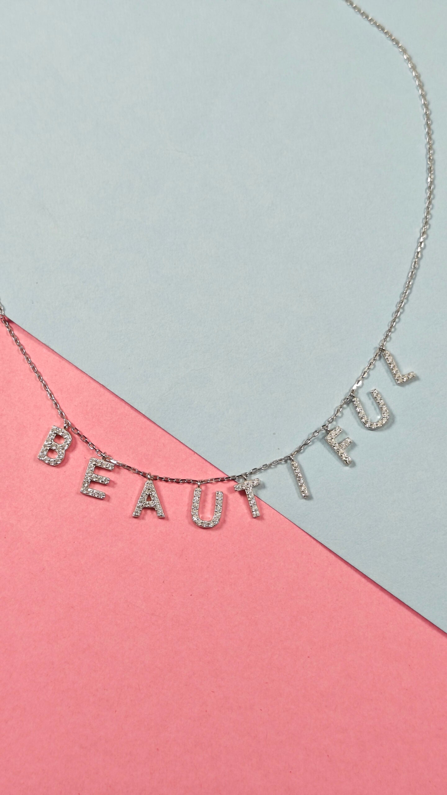 Necklace with 'BEAUTIFUL' lettering on a pink and gray background